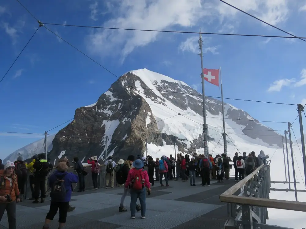 ユングフラウヨッホ展望台から雄大な雪山を望む観光客とスイス国旗。